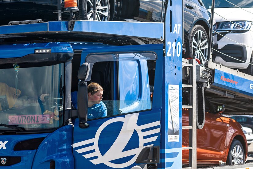 Die Fahrerin dreht sich aus dem Fenster von einem mit Autos beladenem LKW